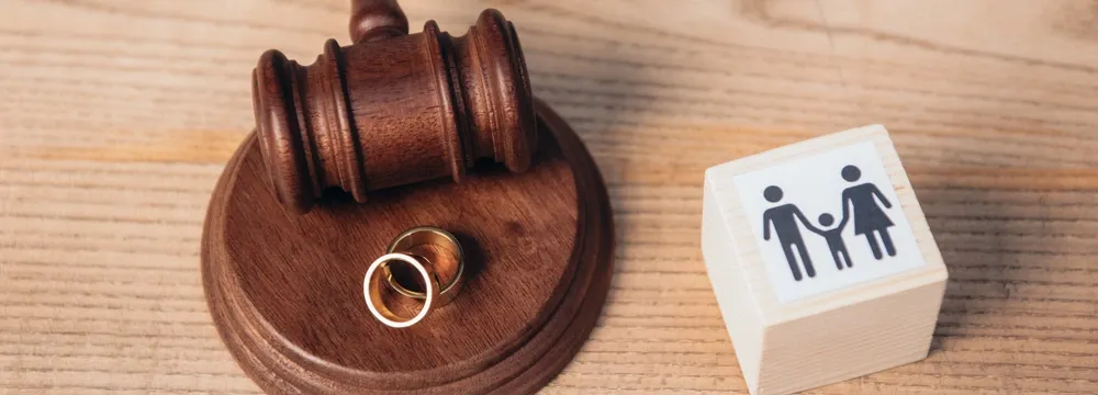 Judge’s gavel resting next to two wedding rings and a wooden block displaying a family icon, symbolizing family law and legal proceedings.