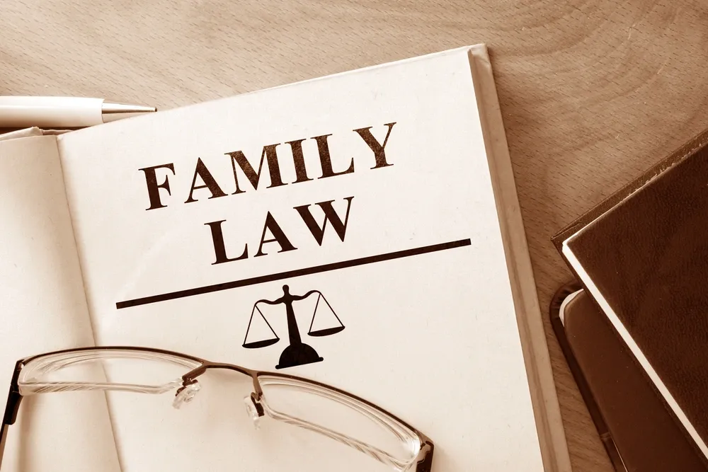 Book titled “Family Law” with a scale of justice icon on the cover, resting on a wooden desk next to eyeglasses and another book, symbolizing legal services for family matters.