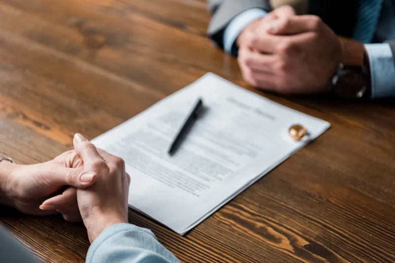 Close-up of two people sitting across from each other at a table with divorce papers, a pen, and wedding rings, representing legal services from a Canadian County divorce attorney.