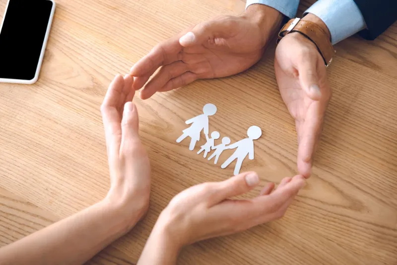 Two people’s hands forming a protective gesture around paper cutouts of a family, symbolizing legal support from a Garvin County family law attorney.